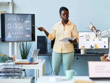 Jeune femme pointant un écran avec des données graphiques tout en l'expliquant à des collègues lors d'une réunion 